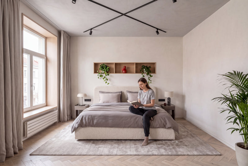 Łóżko tapicerowane Ivi 160x200 w kolorze ecru, tkanina bouclé Fredo – aranżacja sypialni z kobietą siedzącą na łóżku